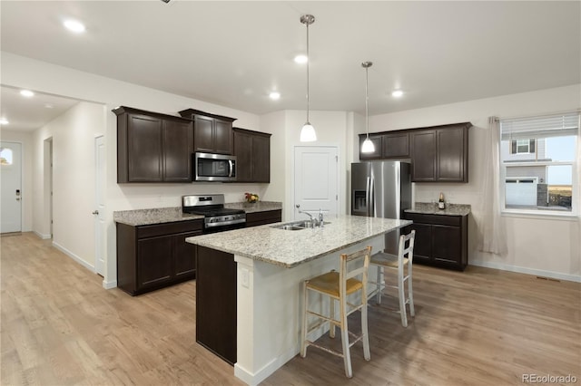 kitchen with light hardwood / wood-style floors, a breakfast bar area, sink, a center island with sink, and appliances with stainless steel finishes