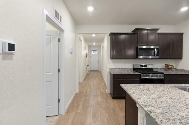 kitchen with dark brown cabinetry, light stone countertops, light hardwood / wood-style flooring, and stainless steel appliances