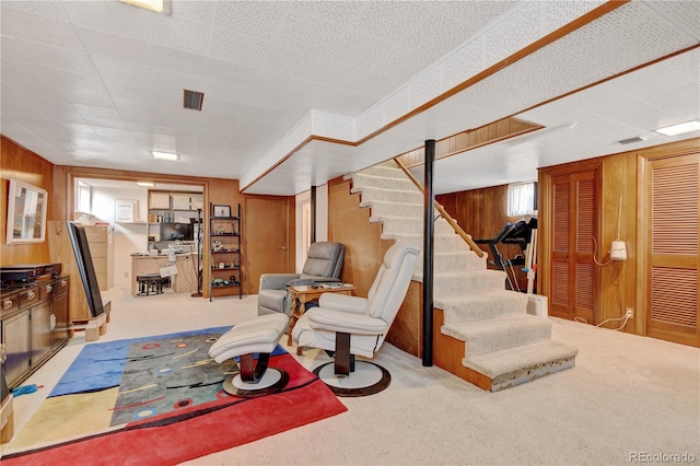 living area featuring wooden walls, stairs, and carpet