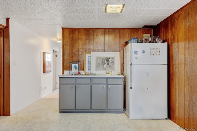 kitchen featuring freestanding refrigerator, gray cabinetry, wooden walls, light countertops, and light carpet