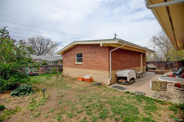 view of side of property with brick siding, fence, and a patio