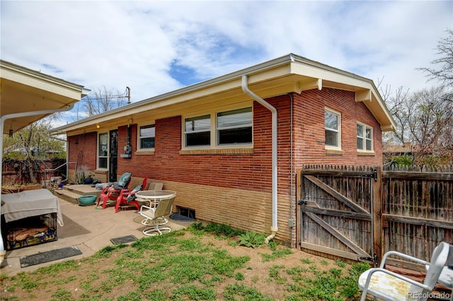rear view of property with a gate, brick siding, fence, and a patio
