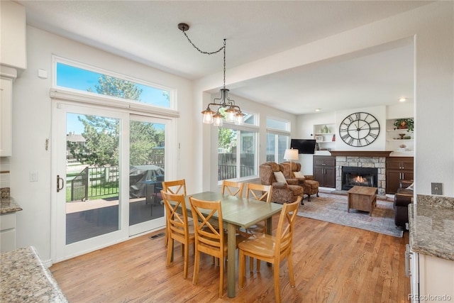 dining room with a stone fireplace, light wood-type flooring, and a chandelier