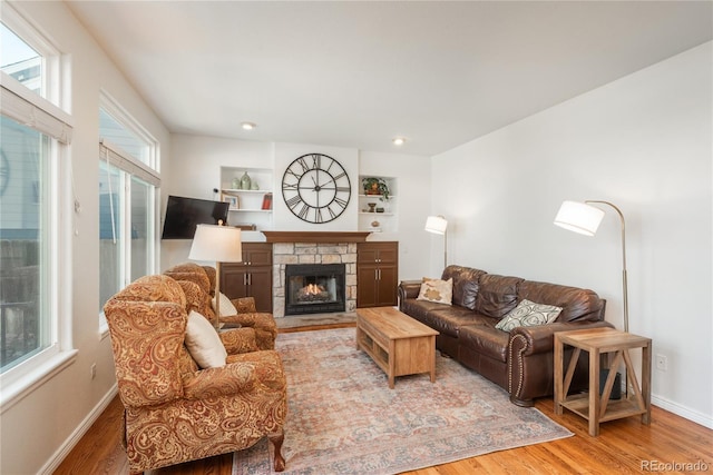 living area with wood finished floors, a stone fireplace, baseboards, and recessed lighting