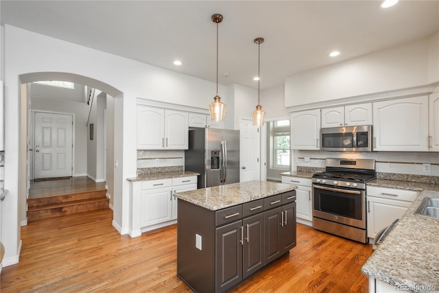 kitchen featuring appliances with stainless steel finishes, arched walkways, white cabinets, decorative backsplash, and pendant lighting