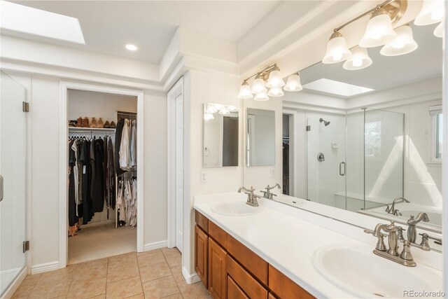 bathroom featuring a shower stall, a walk in closet, tile patterned floors, double vanity, and a skylight
