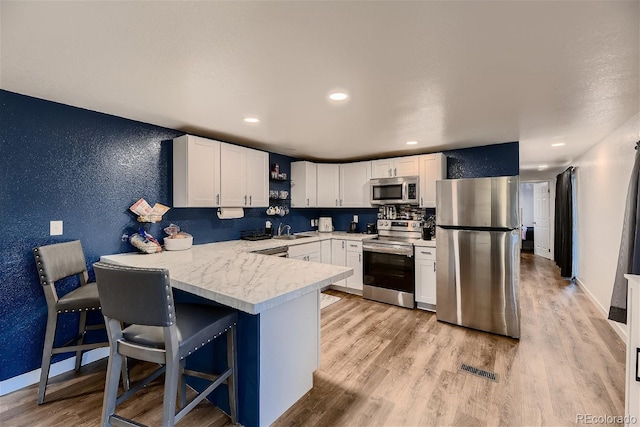 kitchen with sink, stainless steel appliances, a kitchen breakfast bar, light hardwood / wood-style floors, and white cabinets