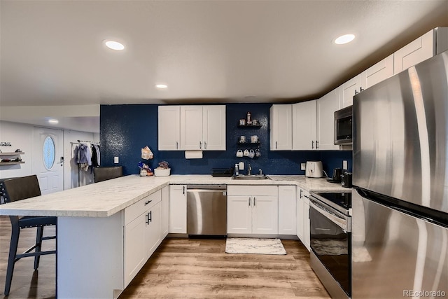 kitchen featuring sink, stainless steel appliances, kitchen peninsula, a kitchen bar, and white cabinets