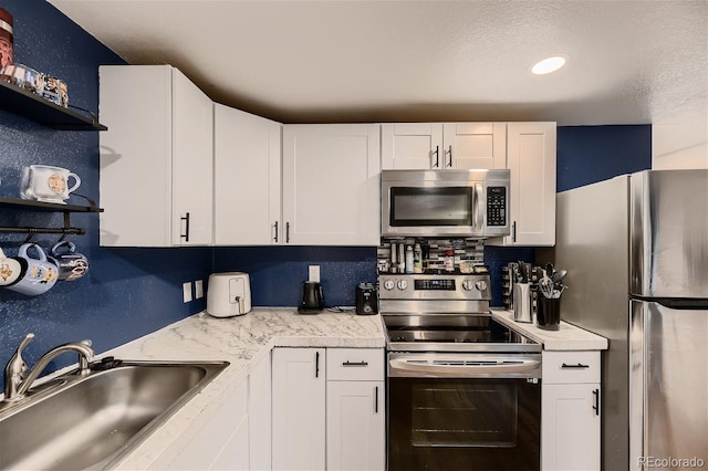 kitchen featuring appliances with stainless steel finishes, a textured ceiling, white cabinetry, and sink