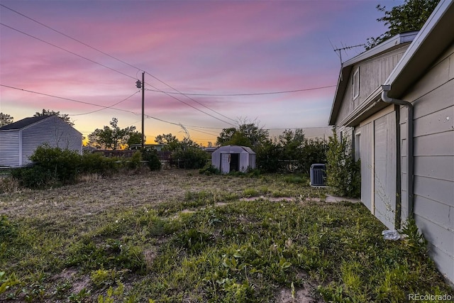 yard at dusk featuring cooling unit and a storage unit