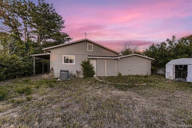 back house at dusk with a shed, a carport, and central air condition unit