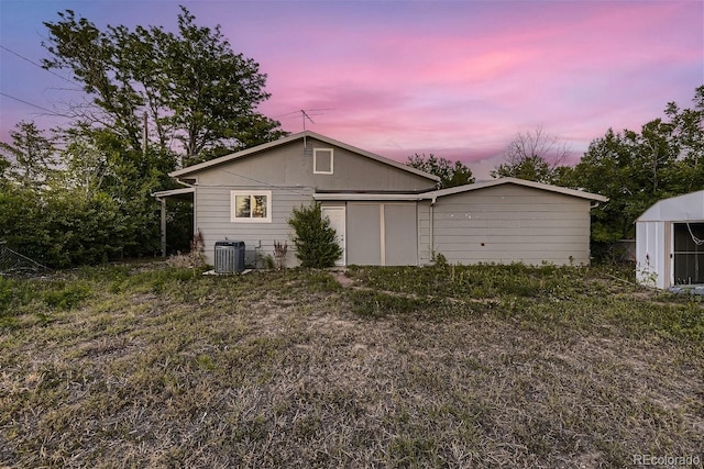 back house at dusk featuring a shed and cooling unit