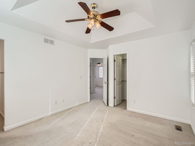 unfurnished bedroom featuring a tray ceiling, ceiling fan, and light colored carpet