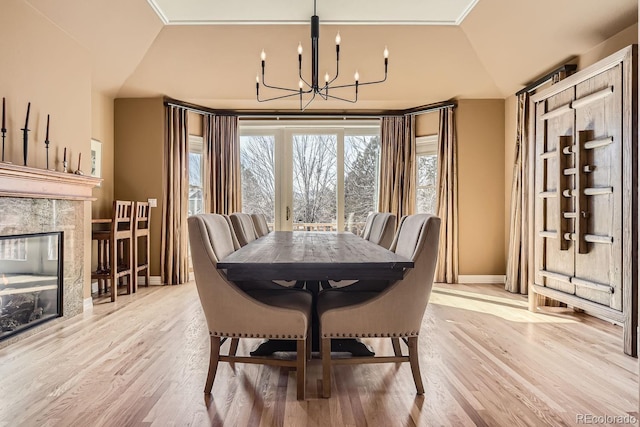 dining area featuring a notable chandelier, lofted ceiling, light wood-style flooring, a premium fireplace, and baseboards