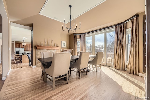 dining area with vaulted ceiling, a notable chandelier, and light wood-style flooring