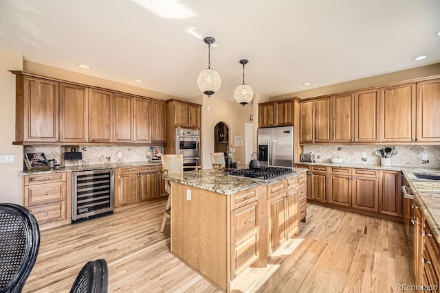 kitchen with light stone counters, wine cooler, brown cabinets, appliances with stainless steel finishes, and light wood-type flooring