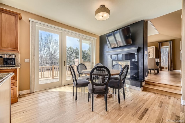 dining room with light wood-type flooring, a multi sided fireplace, and baseboards