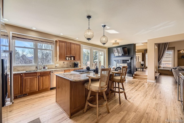 kitchen featuring open floor plan, appliances with stainless steel finishes, brown cabinetry, and a sink