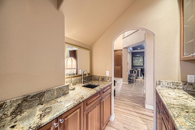 kitchen with arched walkways, light stone counters, a sink, light wood-style floors, and vaulted ceiling