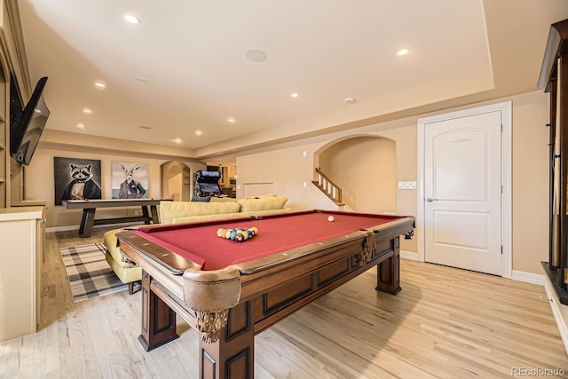 game room with arched walkways, pool table, a raised ceiling, and light wood-style flooring