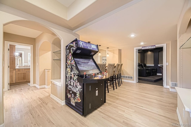 interior space featuring light wood-type flooring, baseboards, visible vents, and arched walkways