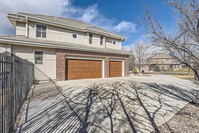 view of front of house featuring a garage, driveway, stucco siding, fence, and brick siding