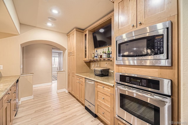6790 W Crestline Ave, Littleton, CO 80123 - kitchen with stainless steel appliances, arched walkways, light wood-style floors, light stone countertops, and light brown cabinetry