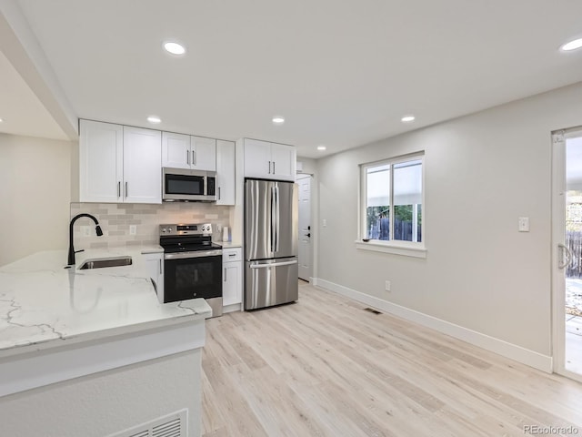 kitchen featuring white cabinetry, sink, stainless steel appliances, light stone counters, and light hardwood / wood-style floors