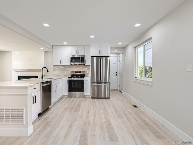 kitchen featuring sink, light hardwood / wood-style flooring, decorative backsplash, appliances with stainless steel finishes, and white cabinetry