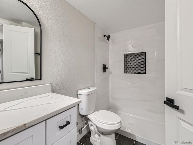 bathroom with a tile shower, tile patterned flooring, vanity, and toilet