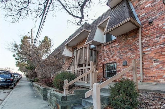 exterior space featuring stairs, brick siding, mansard roof, and roof with shingles