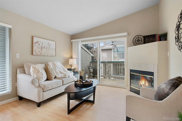 living room featuring lofted ceiling, light hardwood / wood-style floors, a tile fireplace, and a wealth of natural light