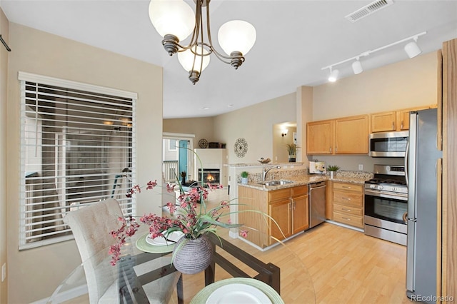 kitchen featuring sink, light stone counters, appliances with stainless steel finishes, kitchen peninsula, and pendant lighting