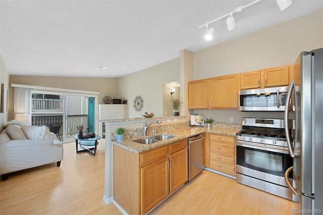 kitchen with sink, light stone counters, light hardwood / wood-style flooring, appliances with stainless steel finishes, and kitchen peninsula