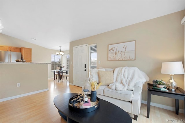 living area featuring an inviting chandelier, baseboards, light wood-type flooring, and lofted ceiling