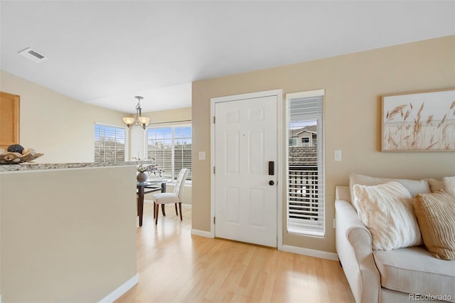 foyer entrance with baseboards, visible vents, light wood finished floors, and a notable chandelier
