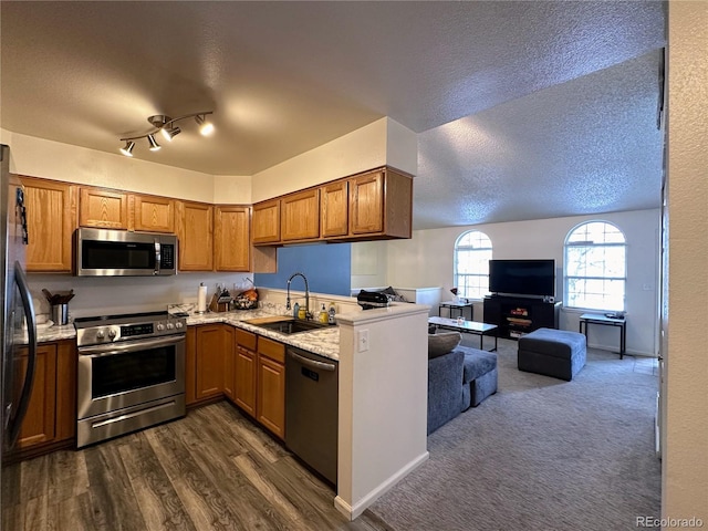 kitchen with brown cabinets, open floor plan, stainless steel appliances, a textured ceiling, and a sink