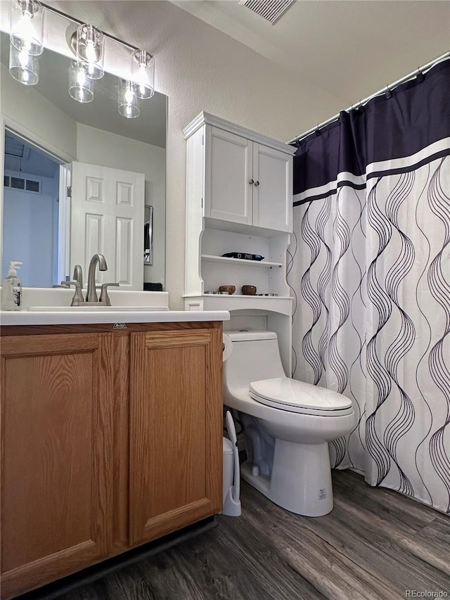 bathroom with visible vents, a textured wall, toilet, wood finished floors, and vanity