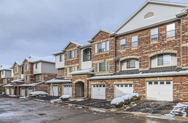 view of property featuring an attached garage, brick siding, a residential view, and driveway