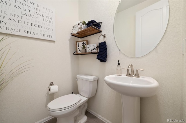 half bathroom featuring baseboards, a sink, and toilet