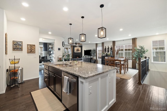 kitchen with stainless steel dishwasher, a kitchen island with sink, dark wood-type flooring, and a sink