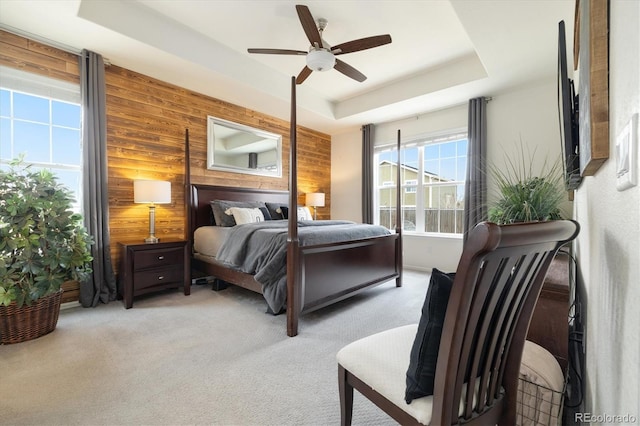 carpeted bedroom with wooden walls, a tray ceiling, and a ceiling fan