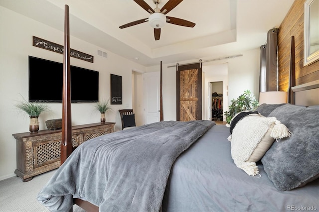 bedroom with a barn door, visible vents, a spacious closet, carpet, and a raised ceiling