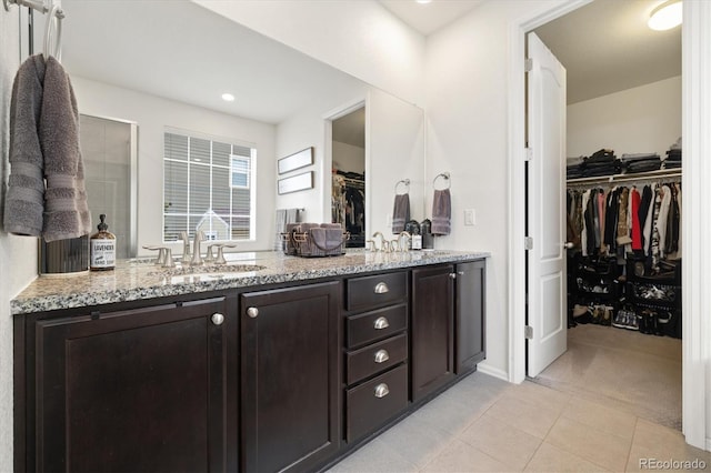 bathroom with double vanity, tile patterned floors, a walk in closet, a shower stall, and a sink