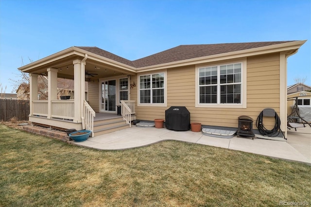 rear view of property with a patio, a shingled roof, a lawn, a ceiling fan, and fence