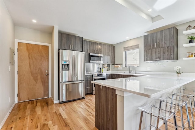 kitchen with dark brown cabinets, a breakfast bar area, kitchen peninsula, light hardwood / wood-style flooring, and appliances with stainless steel finishes