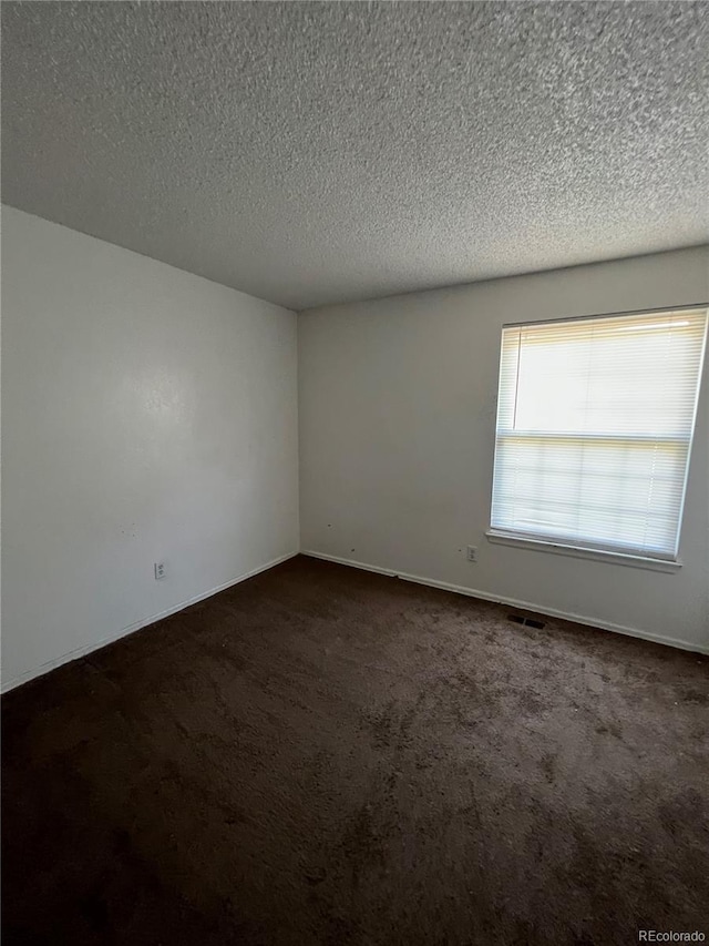 empty room with dark carpet and a textured ceiling