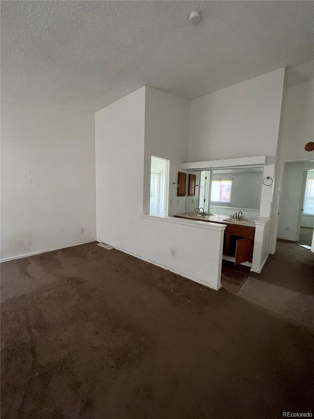 unfurnished living room with dark colored carpet, sink, a textured ceiling, and a high ceiling