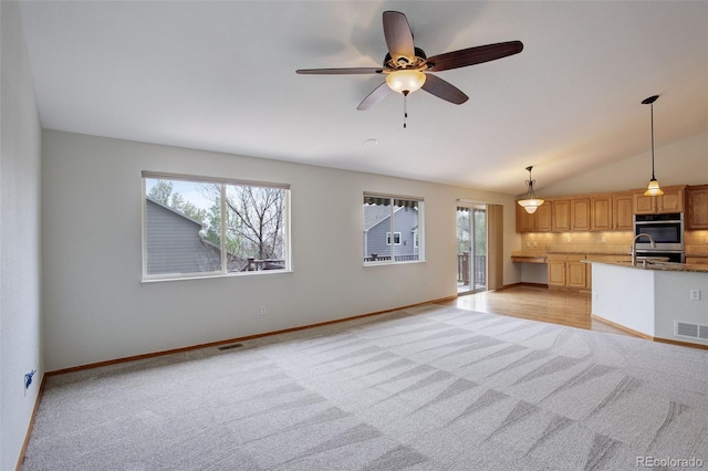 unfurnished living room with light colored carpet, healthy amount of natural light, a ceiling fan, baseboards, and vaulted ceiling