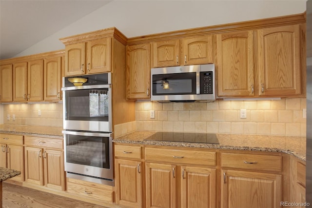 kitchen with appliances with stainless steel finishes, vaulted ceiling, light stone counters, tasteful backsplash, and light wood-style floors